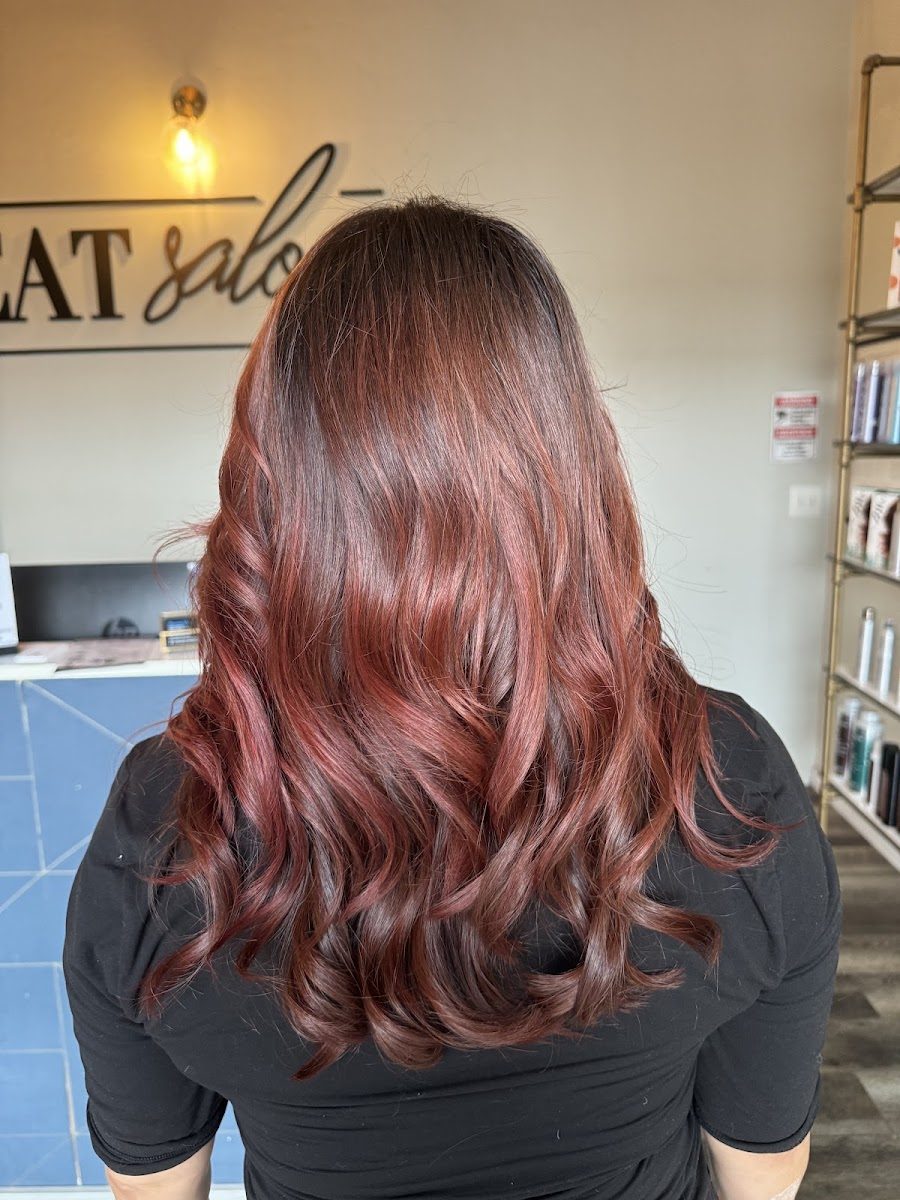 Long copper-red layered waves in front of the Hot Seat Salon wall sign